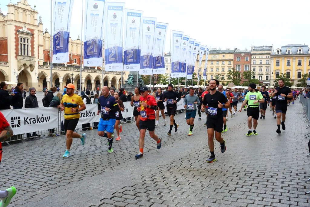 A group of runners participating in a marathon in Kraków, Poland, with historical architecture in the background and banners lining the street.