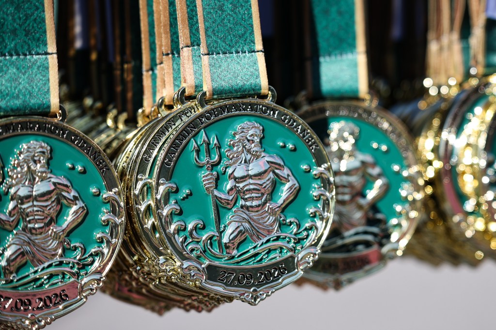 Close-up of decorative medals featuring a muscular figure with a trident, surrounded by waves, hanging on display with green ribbon straps.